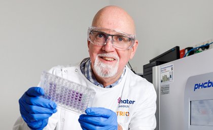 UQ Honorary Professor John Hooper a man in a white coat, glue gloves and glasses holds up a small tray of purple dots